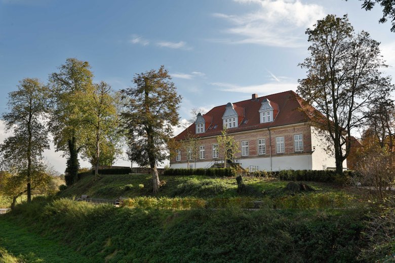 Schloss Landestroste in Neustadt a. Rbge. Blick auf das Schloss landestrost. Das Schlossgebäude steht auf einem grünen Hügel, umrandet von Bäumen.