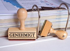 Symbolbild Genehmigung Nahaufnahme eines Aktenordners mit einem Genehmigt-Stempel im Vordergrund
