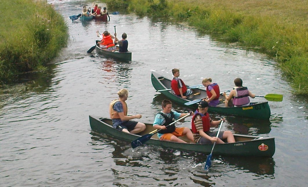 5 Kanus im Wasser mit je drei Jugendlichen an Board. Vogelperspektive