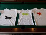 Auf einem Tisch liegen 3 weiße T-Shirts, die mit Flugzeugen, Herzen und Sternen selbst gestaltet wurden