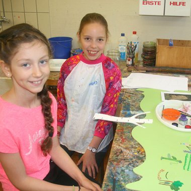 Künstler Bild Bevesen Zwei Mädchen sitzen an einem Künstlertisch vor dem Bild und lächeln in die Kamera