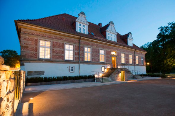 Blick auf den Haupteingang des Schlosses in de Abenddämmerung. Die Fenster sowie die Eingangstreppe sind beleuchtet.