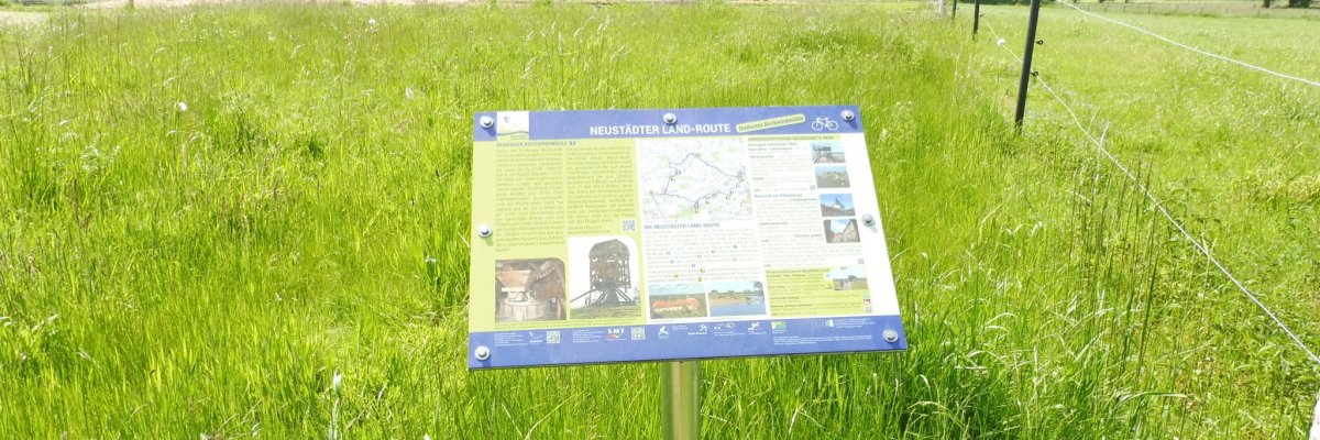 Beispielbild Infotafel Neustädter Landroute Eine Infotafel zur Neustädter Landroute steht vor einer Wiese
