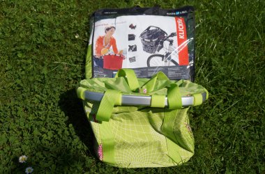 Lenkerkorb grün Ein grüner Korb für den Fahrradlenker steht auf einer grünen Wiese, dahinter ist die Verpackung zu sehen