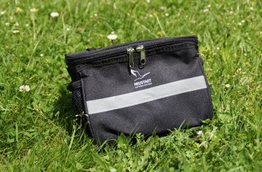 kleine Lenkertasche mit Neustadt-Logo eine kleine shwarze Lenkertasche steht auf einer grünen Wiese, auf der Tasche ist mittig vor das Neustadt-Logo zu sehen