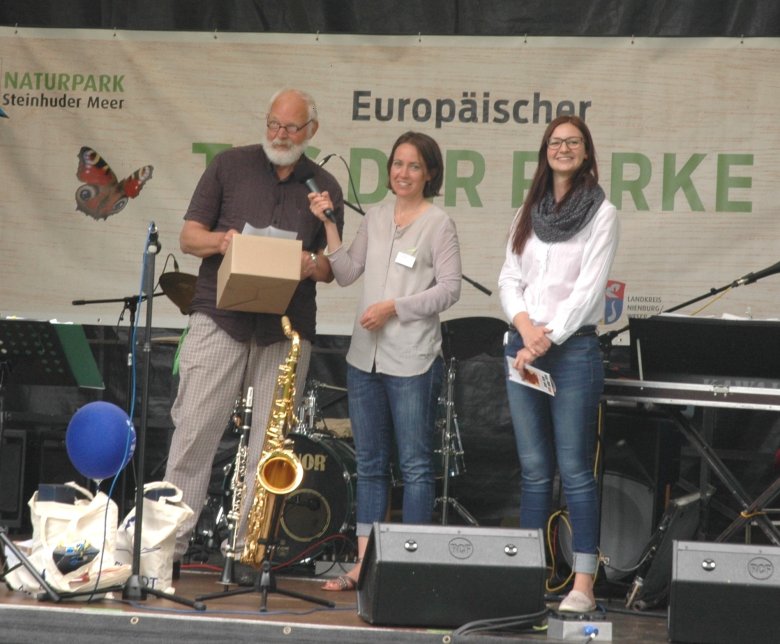 Auf einer Bühne stehen drei Personen. Die Veranstaltung nennt sich Europäischer Tag der Parke