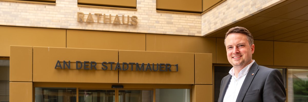 Bürgermeister vorm neuen Rathaus Portrait des Bürgermeisters Dominic Herbst vor dem Eingangsbereich des neuen Rathauses. Die Schriftzüge Rathaus und An der Stadtmauer 1 sind am gebäude zu lesen.
