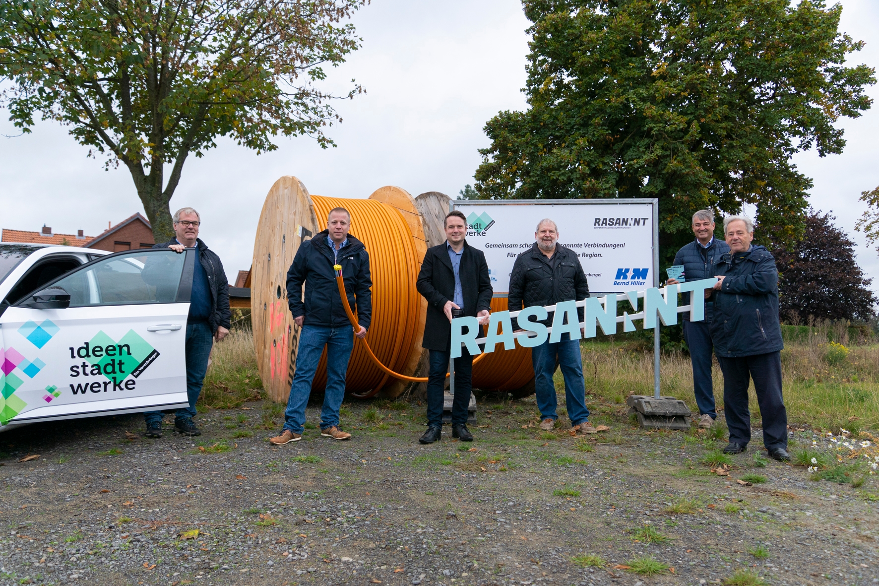 Eine Gruppe von Männern stehen vor großen Kabelrollen mit Glasfaserkabeln. 