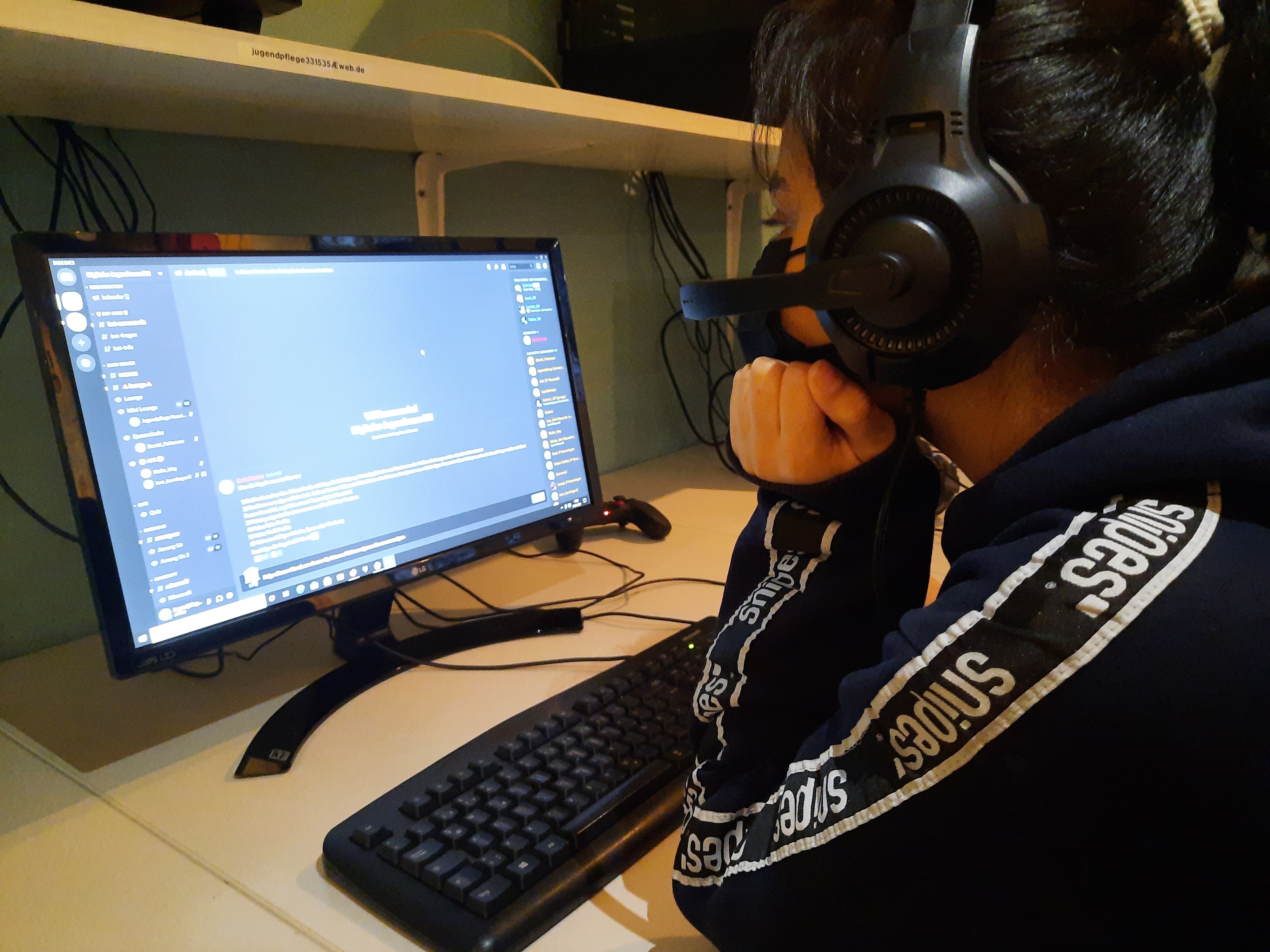Eine Jugendliche sitzt mit Kopfhörern vorm PC-Bildschirm.