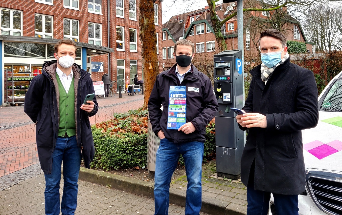 Drei Männer stehen vor einem Parkautomaten und verweisen auf die digitalen Bezahlautomaten.