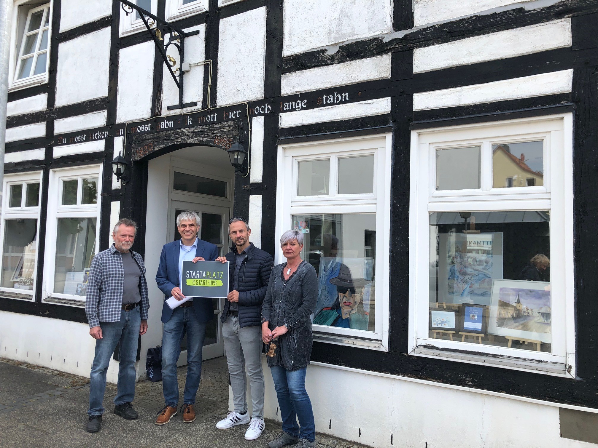 vier Personen stehen vor einem Fachwerkhaus in der Windmühlenstr. 6. Die beiden Herren in der Mitte halten ein Schild hoch, auf dem Start Platz zu lesen ist.