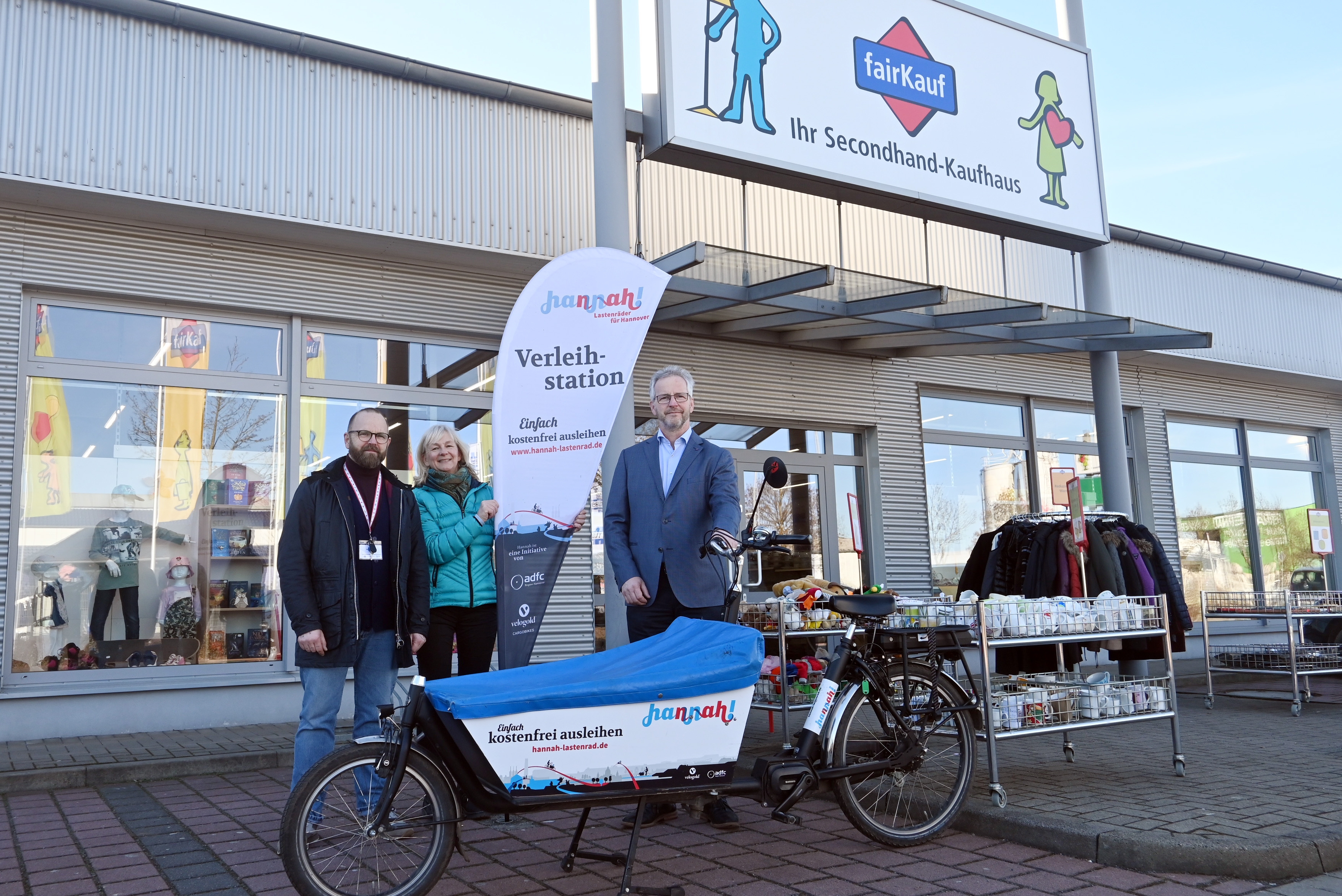 drei Personen stehen vor der fairKauf-Filia in Neustadt. davor steht das Lastenrad Hannah. Alle lächeln in die Kamera