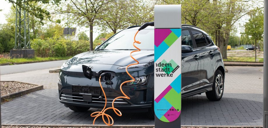 Symbolbild Carsharing Stadtwerke Ein schwarzes E-Auto steht auf einem Parkplatz und ist an eine E-Ladesäule der Ideenstadtwerke angeschlossen.