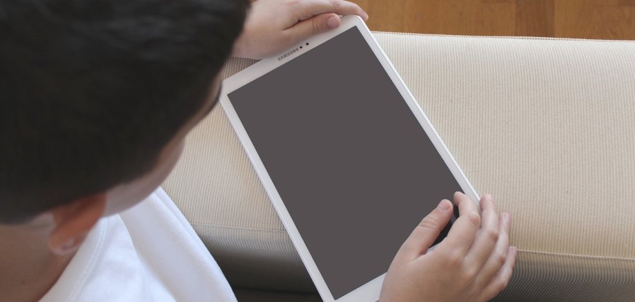 Symbolbild Kinder Mediennutzung Nahaufnahme eines Kindes, das ein weißes tabelt ind er Hand hält und darauf schaut.