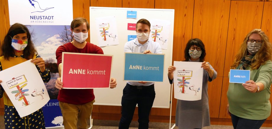 Pressefoto Frühe Hilfen Fünf Personen halten Plakate in die Kamera, auf denen steht Anne kommt. Alle tragen einen Mund-Nasen-Schutz.