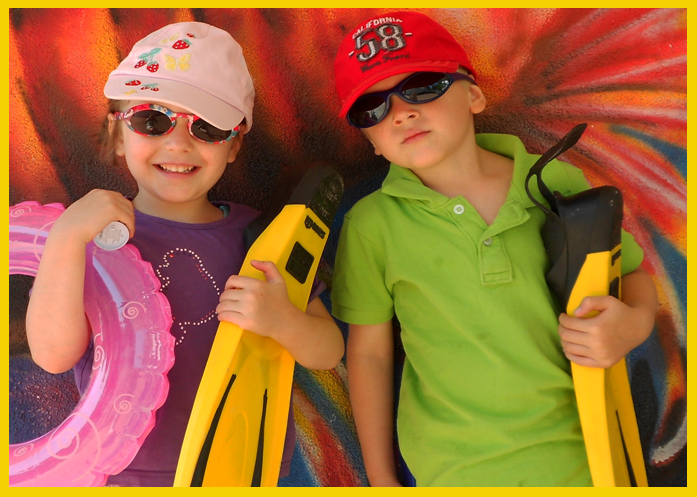 Kinderferienpass Gelber Rahmen. Zwei Kinder mit Sonnenbrillen, Schwimmreifen und Taucherflossen.