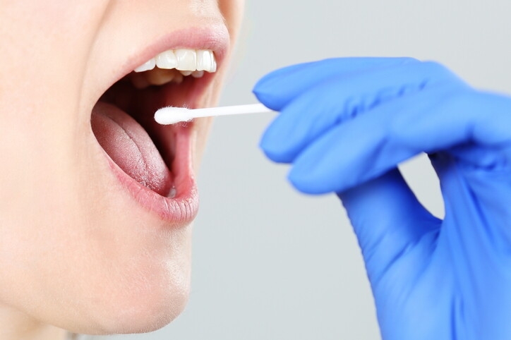 Frau nimmt mit einem Stäbchen eine Speichelprobe für einen Test.
