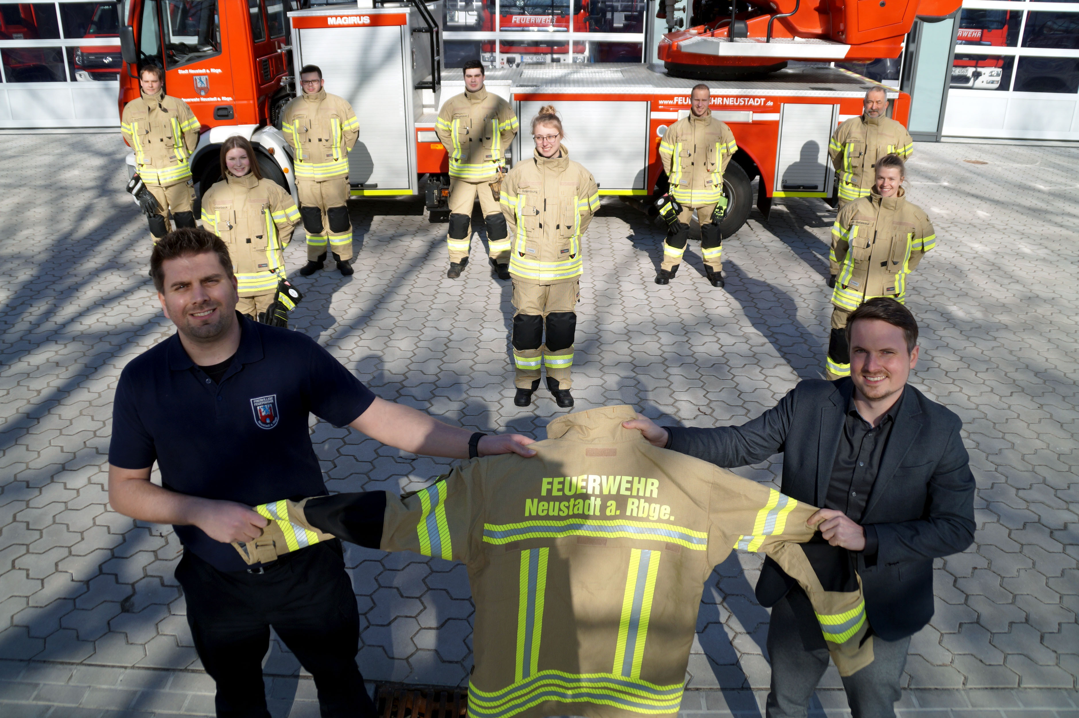vorn rechts Torben Klingemann mit Bürgermeister Dominic Herbst. Im Hintergrund präsentieren Feuerwehrleute aus dem ganzen Stadtgebiet ihre neue Ausrüstung. In der mittleren Reihe von links: Sara Storbeck (FW Eilvese), Ida Schom-burg (FW Nöpke) und Rabea Hatesaul (FW Nöpke). In der hinteren Reihe von links: Dennis Schumann (FW Eilvese), Jan Wiegand (FW Poggenhagen), Luis Neugebauer (FW Bordenau), Alessandro Stade (FW Esperke) und Manfred Walter (FW Laderholz). (c) Stadt Neustadt a. Rbge.de  