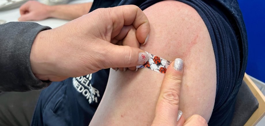 Corona-Impfung Nahaufnahme einer Impfsituation. Ein Mann hat den linken Oberarm frei gemacht, eine Frau klebt ein Pflaster auf die Einstichstelle.