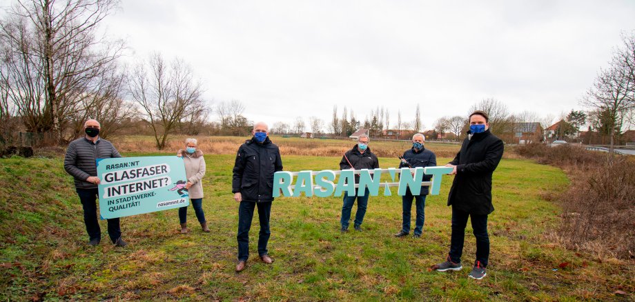 Glasfaserausbau in Empede beginnt im April 6 Personen stehen auf einer Weise. Sie halten ein Werbebanner und den Schriftzug Rasannnt in die Höhe. Alle tragen einen Mund-Nasen-Schutz.