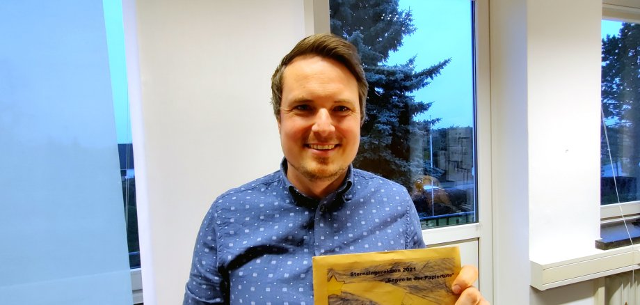 Sternsingeraktion 2021 Bürgermeister Dominic Herbst hält einen bemalten Briefumschlag in die Kamera. Darauf steht Sternsingeraktion 2021 "Segen in der Papiertüte"