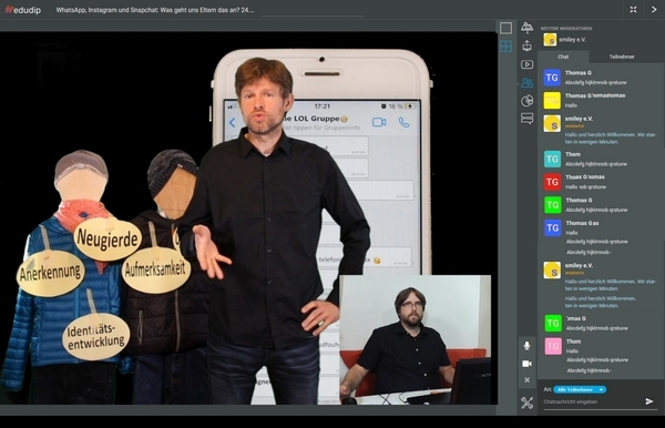 Screenshot eines Online-Seminars. Ein Mann steht vor einem übergroßen handy, links von ihm ein Schaubild. Unten rechts ist ein weitere Bildausschnitt mit einem weiteren Mann mit Headset am PC.