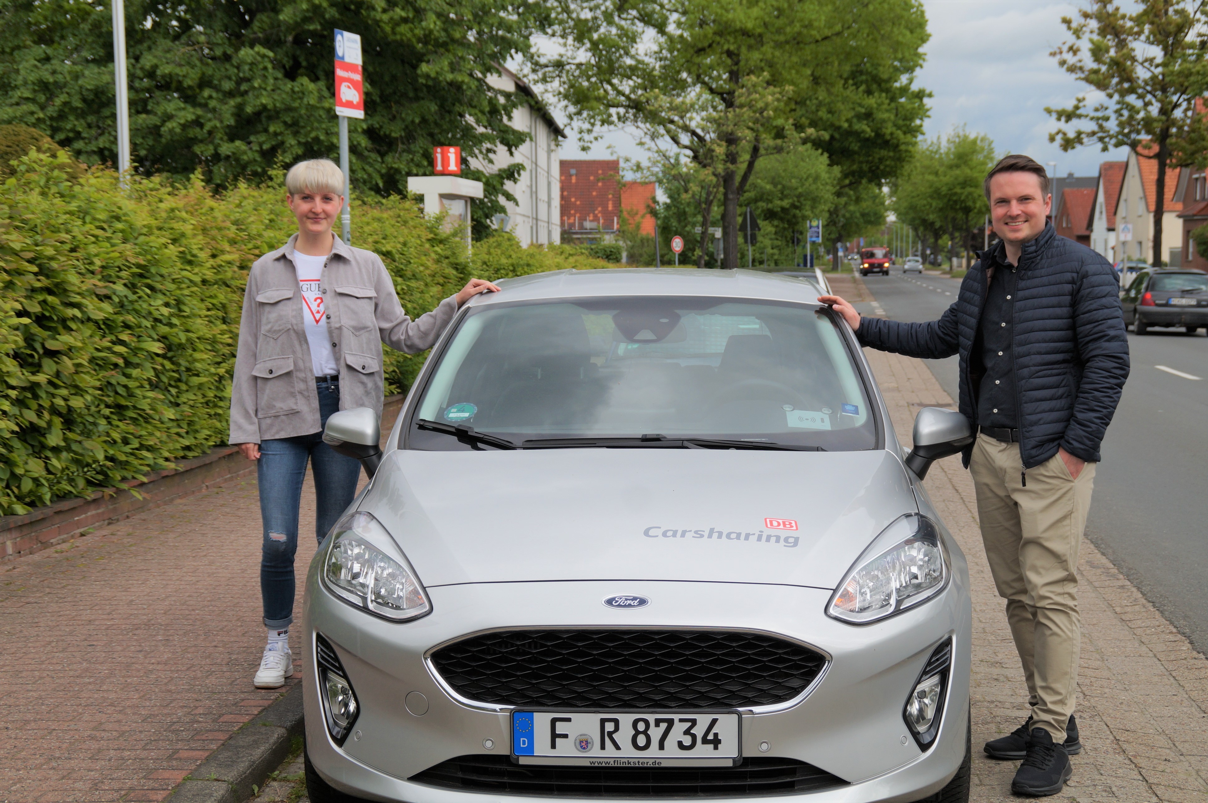 Neustadts Bürgermeister Dominic Herbst (links) und die Klimaschutzmanagerin Wendy Pfeil (links) werben für die Gutscheinaktion von Flinkster. Die beiden Personen stehen links und rechts neben einem Flinksterwagen an der Nineburgser Str. 31.