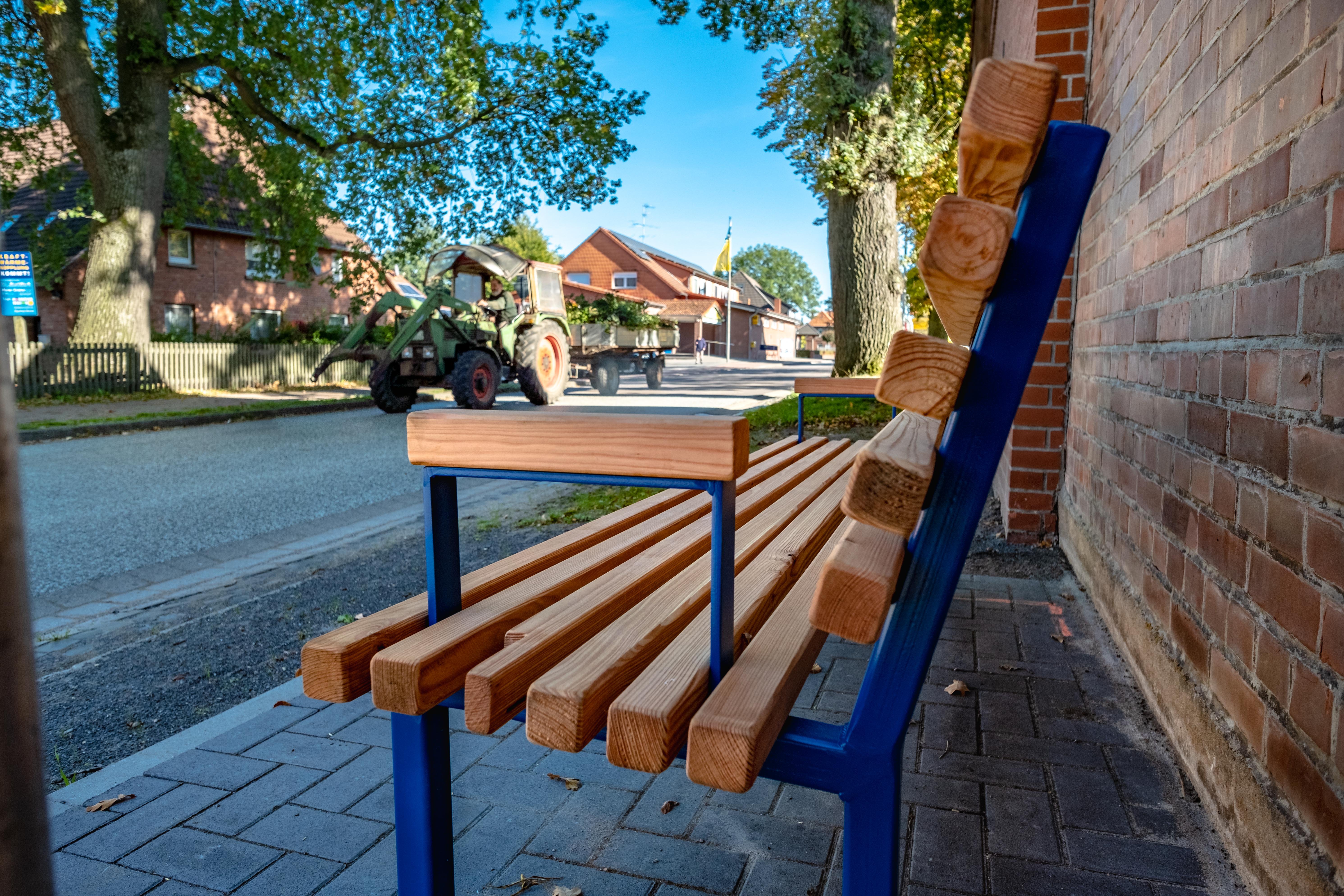Nahaufnahme einer Holzbank mit blauem Gestell, das Foto ist von der Seite aufgenommen. 