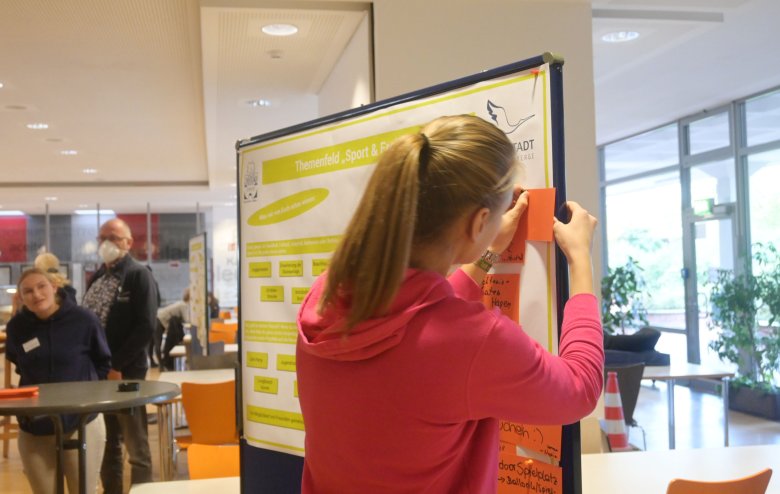 Jugendbeteiligung KGS Mitmach-Aktion Ein junges Mädchen pinnt eine Karte mit Ideen an eine Stellwand.