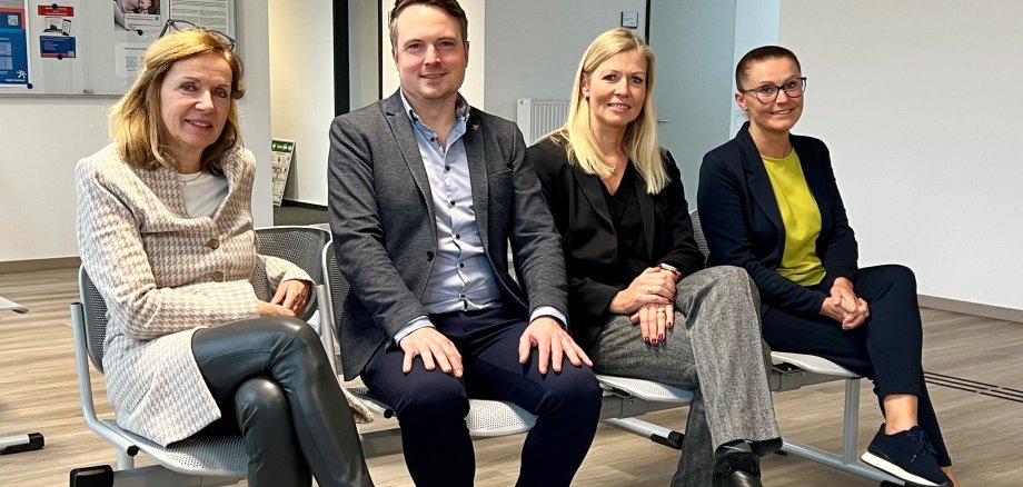 Pressefoto JocCenter NeustadtTor Vier Personen sitzen im Wartebreich des neuen JobCenters auf einer Bank. Alle Lächeln in die Kamera