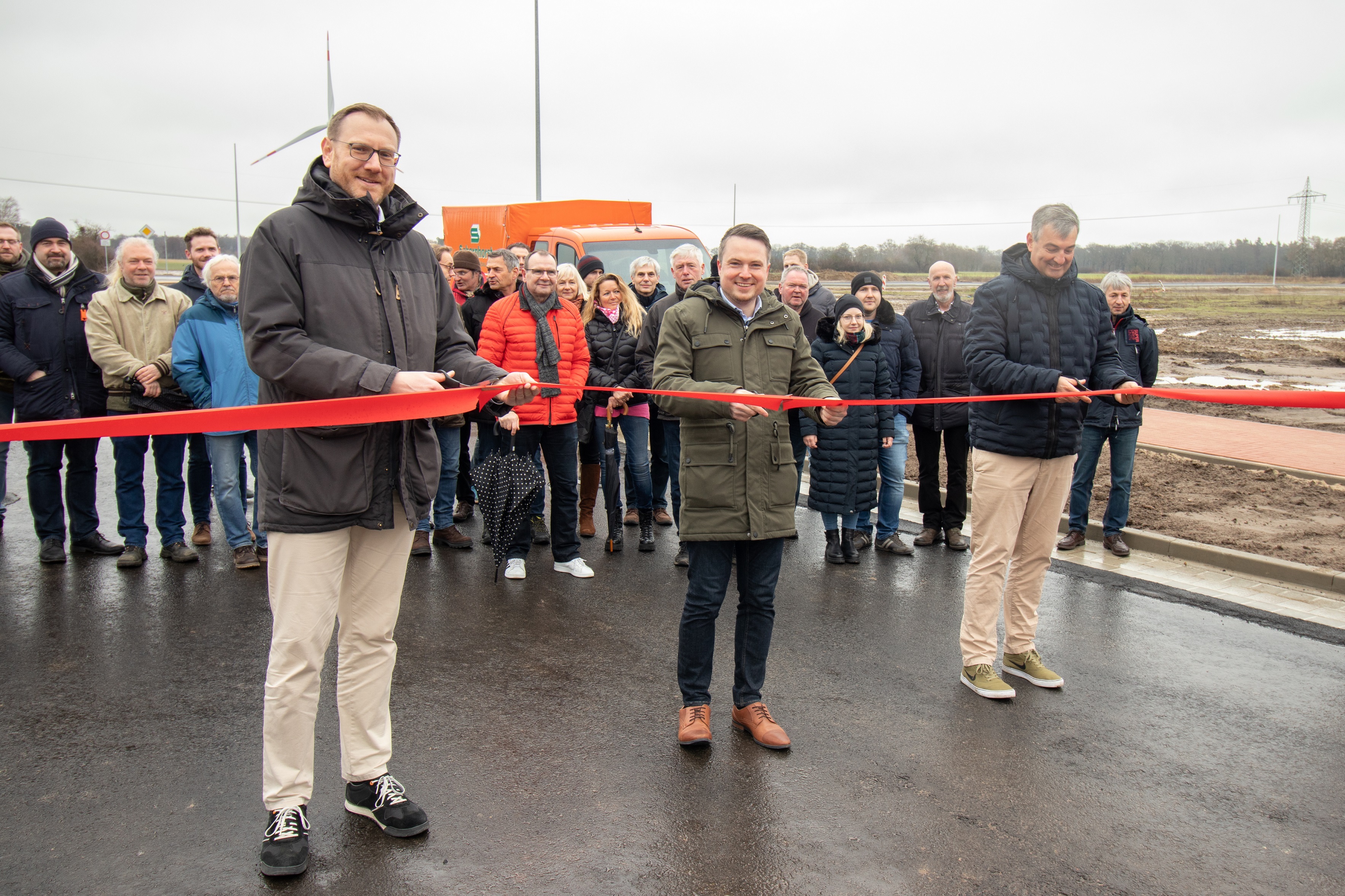 (v.l.) Thomas Reimann, Projektleiter für das Gebiet und Prokurist im Ideenstadtwerke Konzern, Bürgermeister Dominic Herbst und Ideenstadtwerke-Geschäftsführer Dieter Lindauer schneiden das symbolische rote Band zur Einweihung des neuen Gewerbegebiets durch. Im Hintergrund freuen sich Aufsichtsratsmitglieder, Käuferinnen und Käufer, beteiligte Unternehmen sowie Mitarbeiterinnen und Mitarbeiter der Stadt sowie der Ideenstadtwerke.