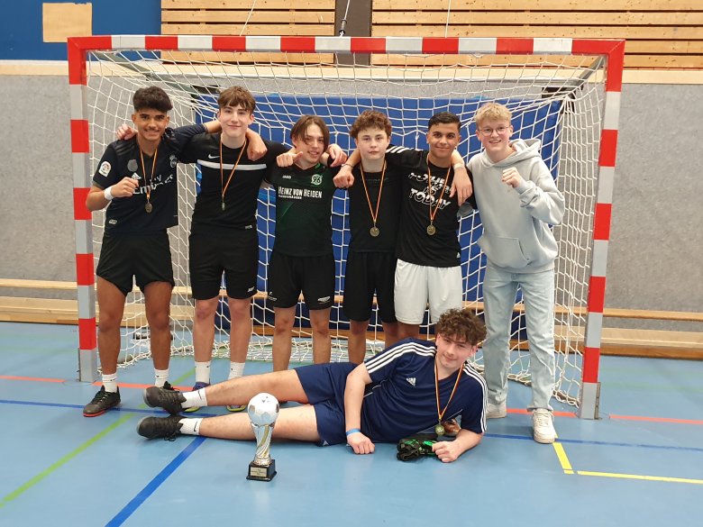 Siegermannschaft Neustädterfußball Cup 2023 Das Siegrteam des Turnier. Sechs Jugendliche stehen vor dem Tor, ein siebter liegt davor. Vorne steht de Siegerpokal des Turniers. Alle freuen sich und lächeln in die Kamera.