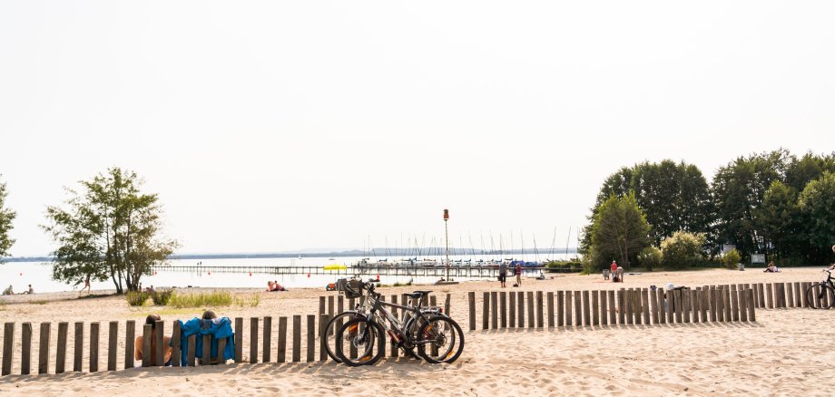 Badestrand in Mardorf Blick auf den Badestrand am Steinhuder meer in mardorf. Zwei Fahrräder stehen angeschlossen an Holpollern. im Hintergrund ist das Steinhuder Meer sowie einzelne Badegäste erkennbar.