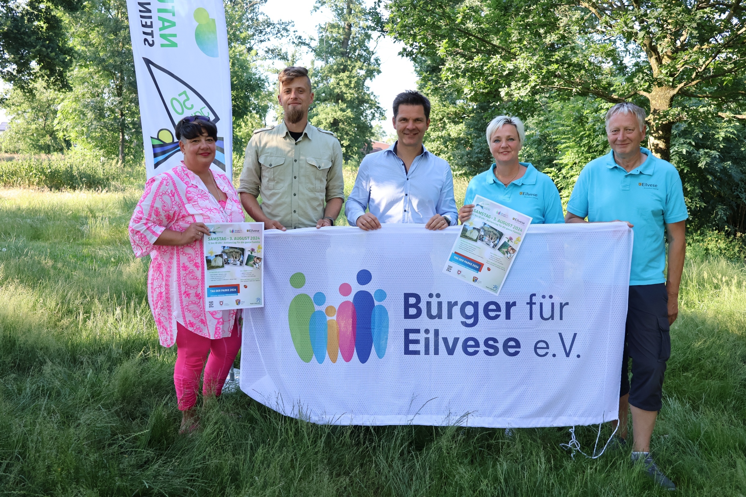 5 Personen stehen auf einer grünen Wiese und halten ein weißes Banner in den Händen. Dort steht Bürger für Eilvese e.V. Sie blicken alle in die Kamera