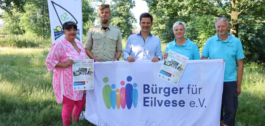 5 Personen stehen auf einer grünen Wiese und halten ein weißes Banner in den Händen. Dort steht Bürger für Eilvese e.V. Sie blicken alle in die Kamera