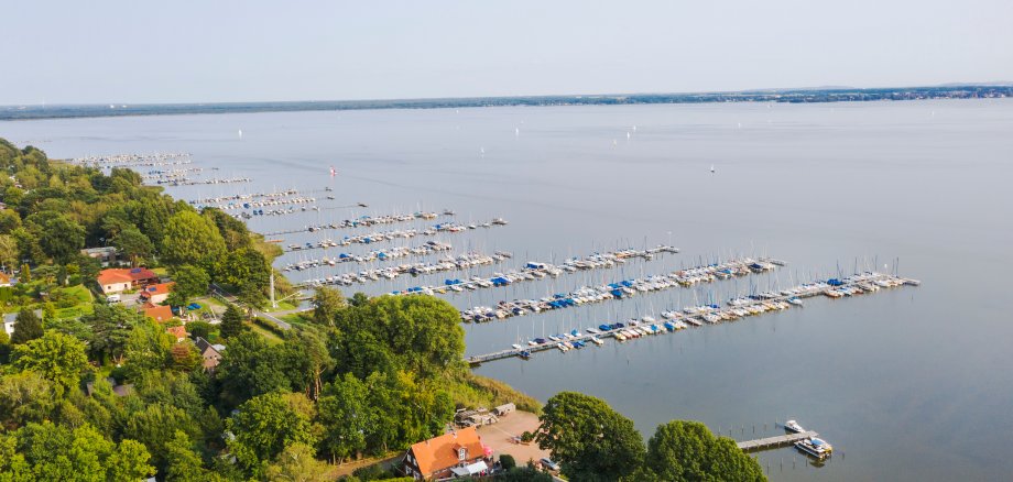 Foto aus der Vogelperspektive, links en Wald mit Häusern und rechts das Steinhuder Meer mit Bootsanlegern