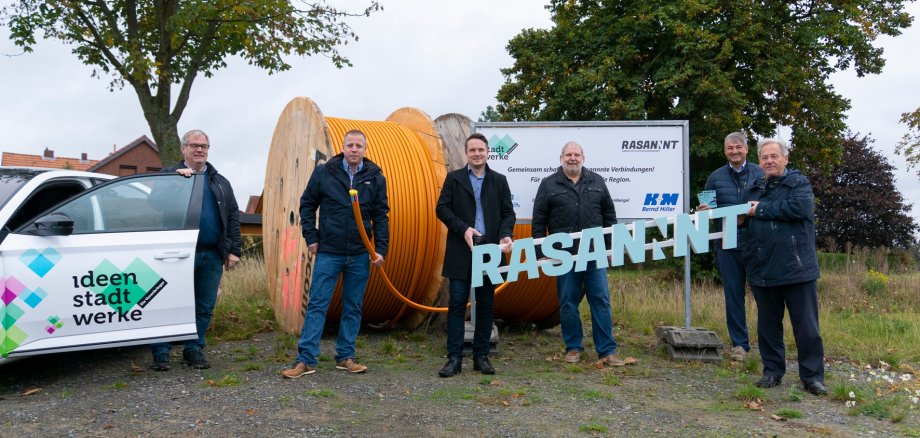 Eine Gruppe von Männern stehen vor großen Kabelrollen mit Glasfaserkabeln. 