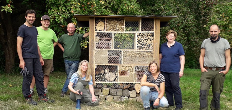 Ein Insektenhotel steht auf einer Wiese. Drum herum stehen und hocken die Mitarbeitenden des Fachdienstes Stadtgrün der Stadt Neustadt a. Rbge.