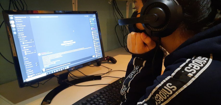 Eine Jugendliche sitzt mit Kopfhörern vorm PC-Bildschirm.