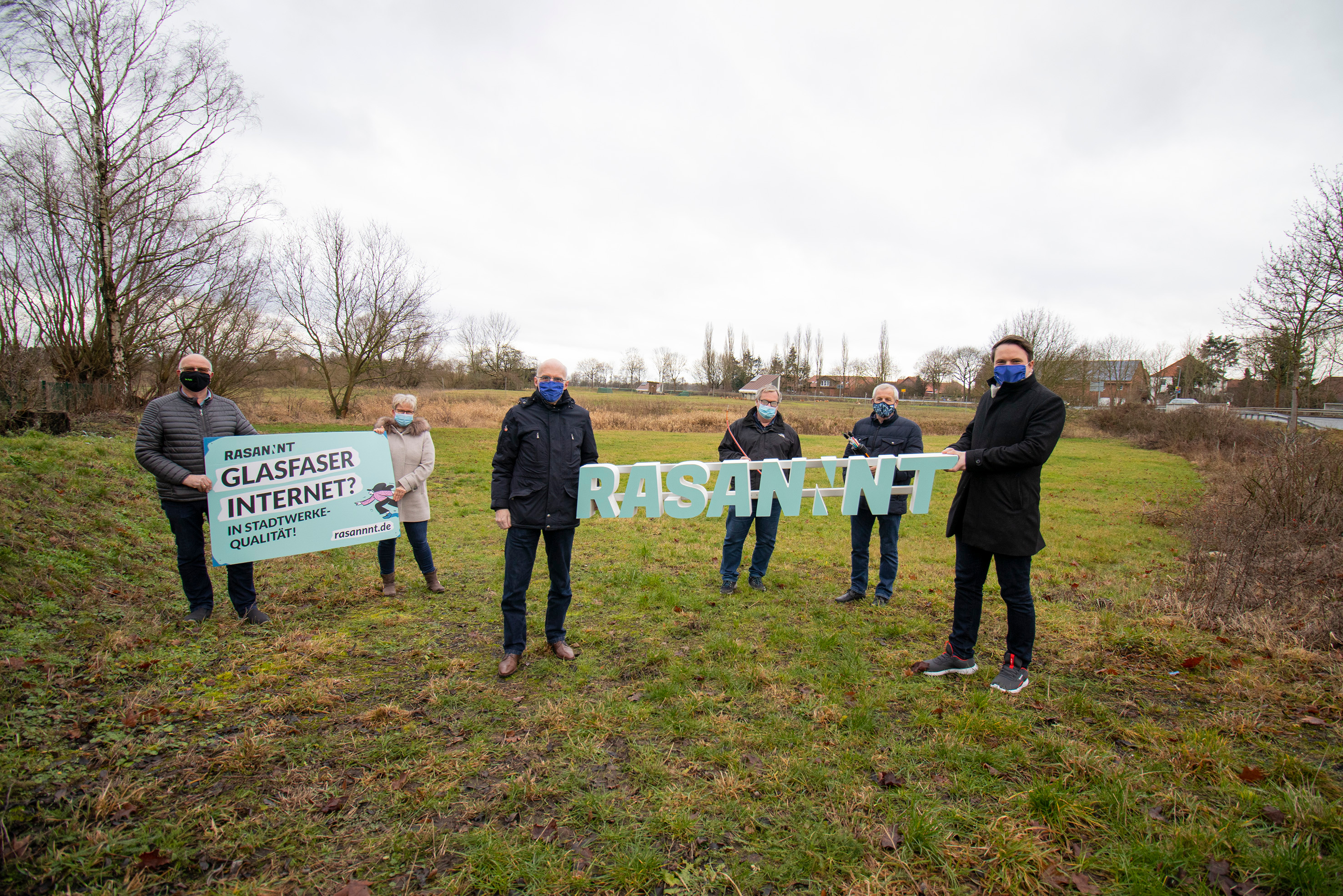 6 Personen stehen auf einer Weise. Sie halten ein Werbebanner und den Schriftzug Rasannnt in die Höhe. Alle tragen einen Mund-Nasen-Schutz.