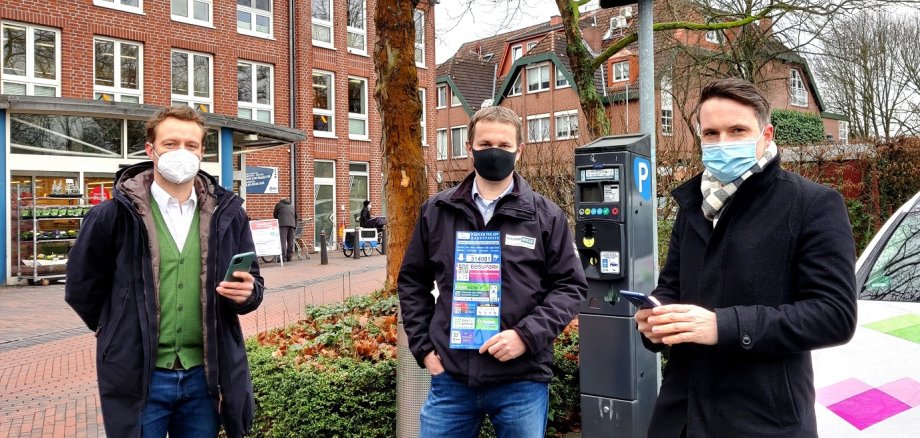 Drei Männer stehen vor einem Parkautomaten und verweisen auf die digitalen Bezahlautomaten.