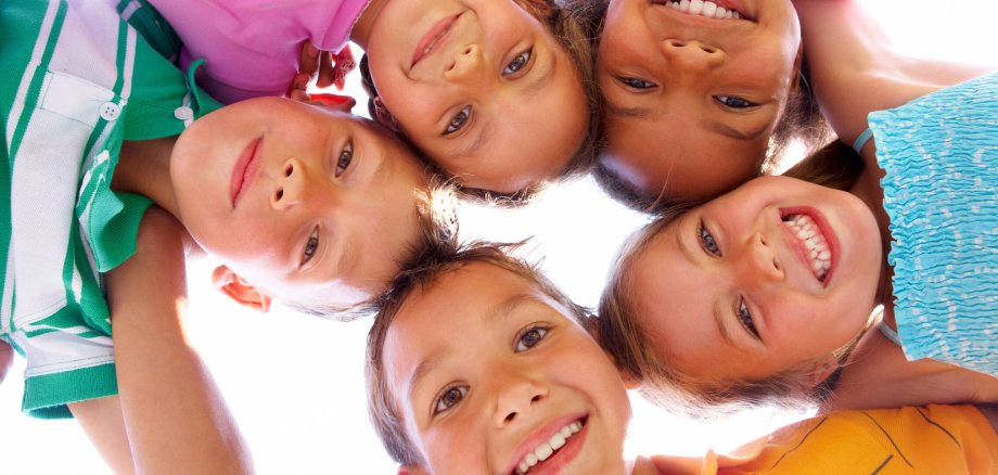 Fünf Kinder stehen im Kreis und gucken von oben in die Kamera.