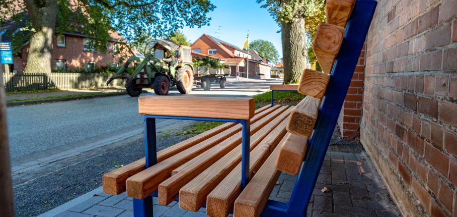 Nahaufnahme einer Holzbank mit blauem Gestell, das Foto ist von der Seite aufgenommen. 