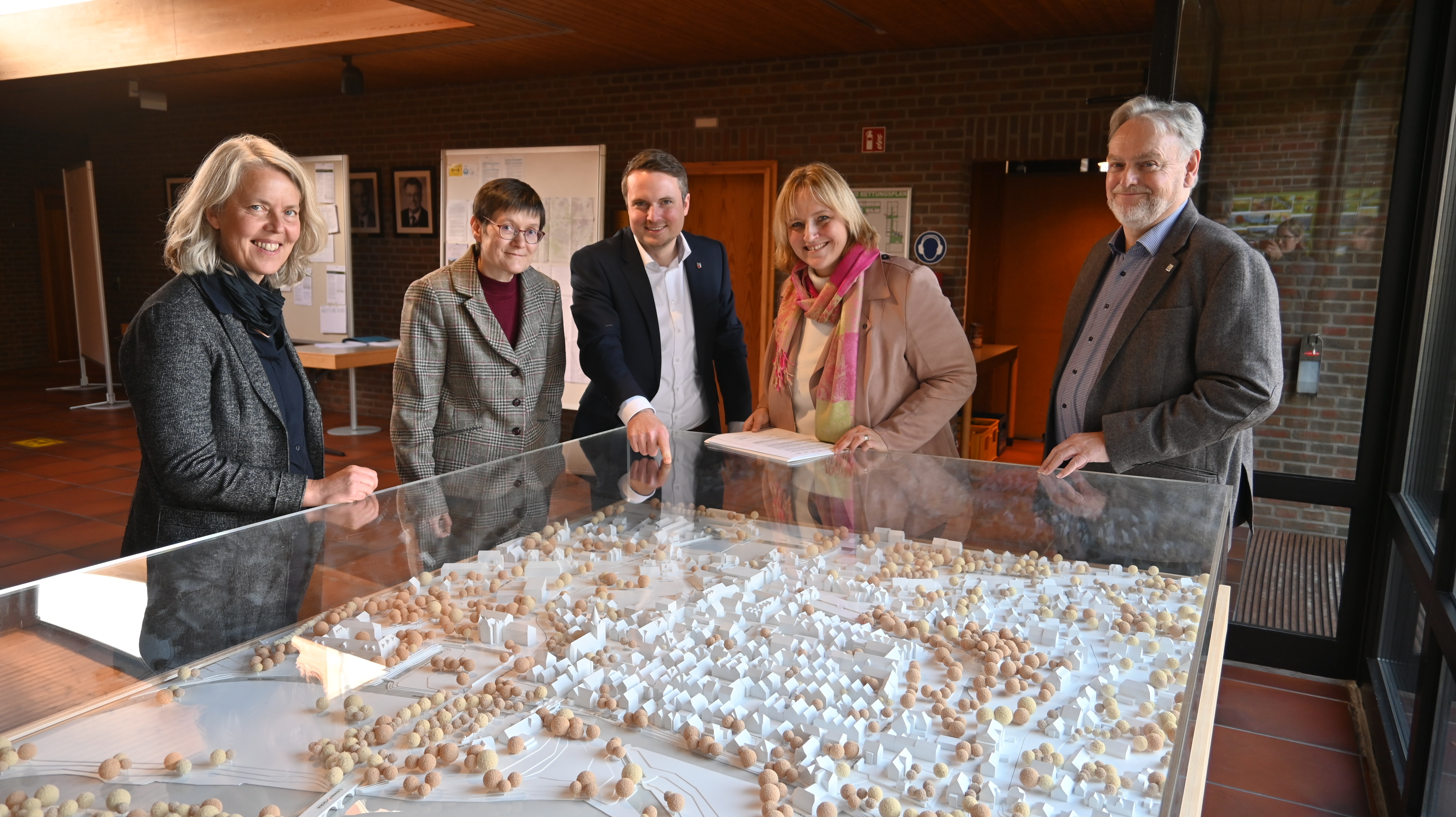 Fünf Personen stehen vor dem Modell der Neustädter Innenstadt im Foyer vor dem Sitzungssaal und lächeln in die Kamera.