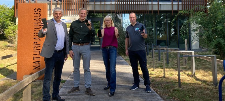 Vier Personen stehen vor dem Naturparkhaus in mardorf. Alle lächeln und halten ihre Handys Richtung Kamera.