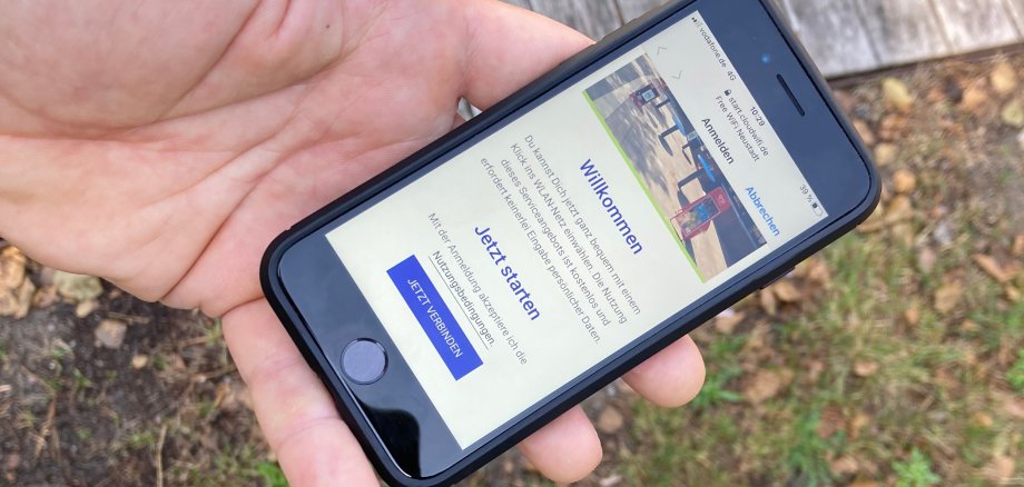Nahaufnahme einer Hand, die ein Handy hält. Man kann den Bildschirm erkennen, auf dem die Startseite zum neuen WLAN-Hotspot zu sehen ist.