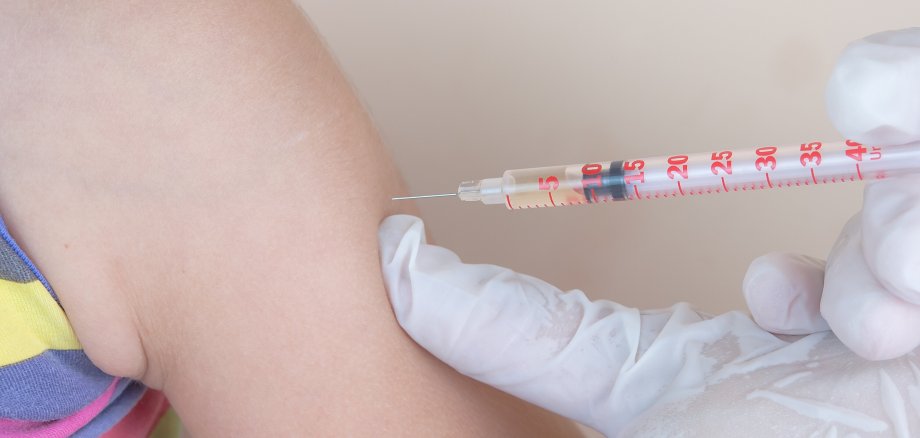 Nahaufnahme einer Impfsituation. Ein Kind bekommt eine Spritze in den Oberarm gesetzt.
