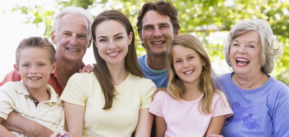 Eine Familie mit vier Erwachsenen und zwei Kindern posiert für ein Gruppenfoto und alle Personen lächeln in die Kamera.