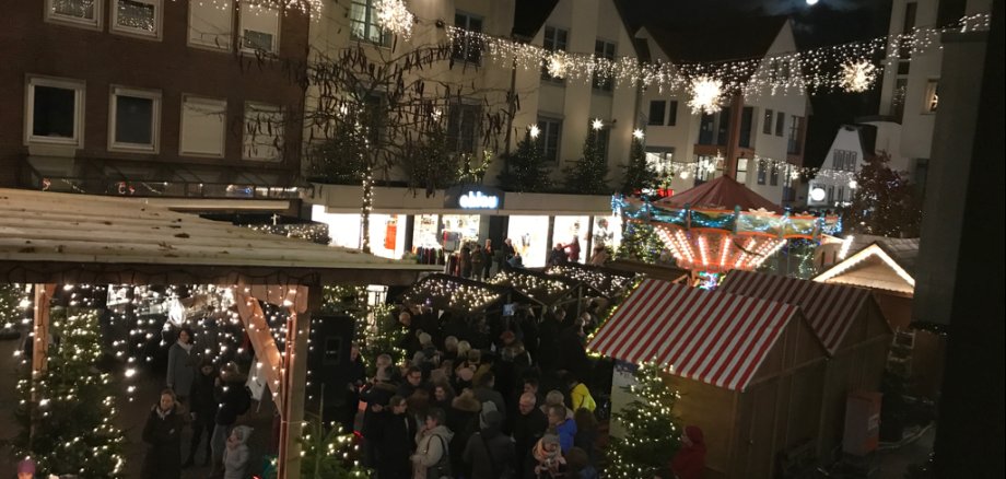 Blick von oben auf den Weihnachtsmarkt in der Marktstr. auf Höhe des Sparkassenvorplatzes. Zu sehen sind Buden und Tannenbäume. Dazwischen zahlreiche Menschen. 