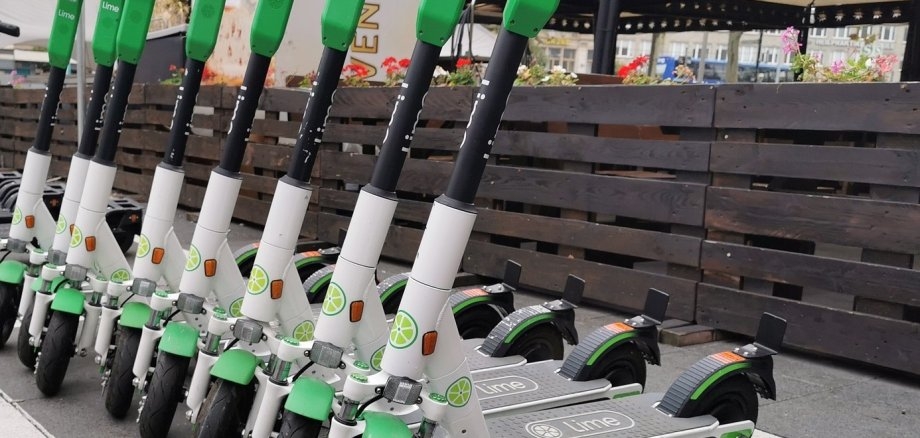 Aufnahme von E-Scooter der Firma Lime. Es stehen mehrere Scooter nebeneinander an einem Straßenrand.